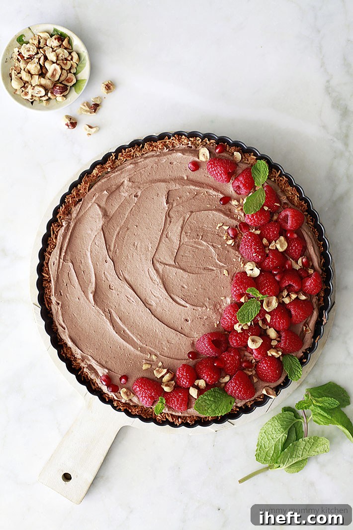 Exquisite vegan coconut chocolate mousse pie, garnished with fresh raspberries and crunchy hazelnuts, ready to be served.