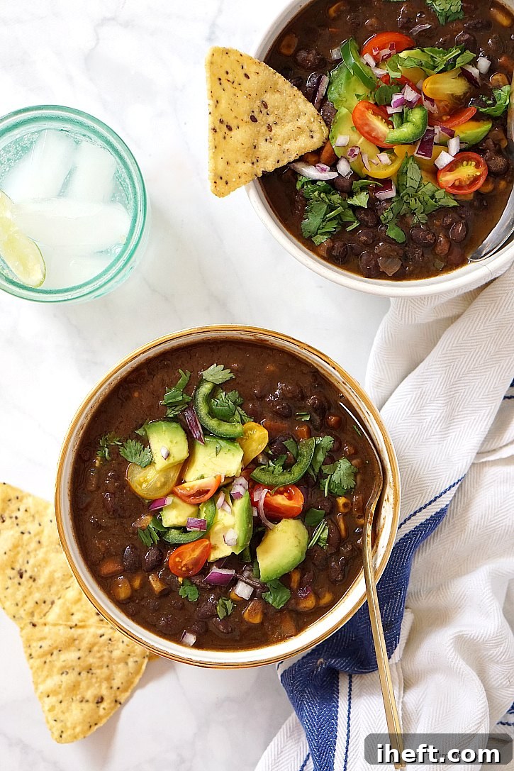 Two bowls of savory black bean soup, generously topped with fresh avocado slices, diced red onions, and ripe tomatoes, ready to be enjoyed.