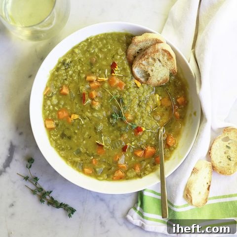 A bowl of rich, green vegetarian split pea soup, beautifully garnished with fresh herbs and served alongside crusty bread, inviting a comforting meal.