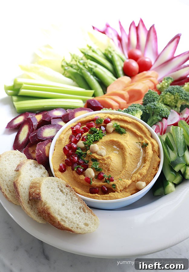 A beautifully arranged platter of pumpkin hummus served with a variety of colorful fresh vegetables, perfect for a healthy Halloween snack.