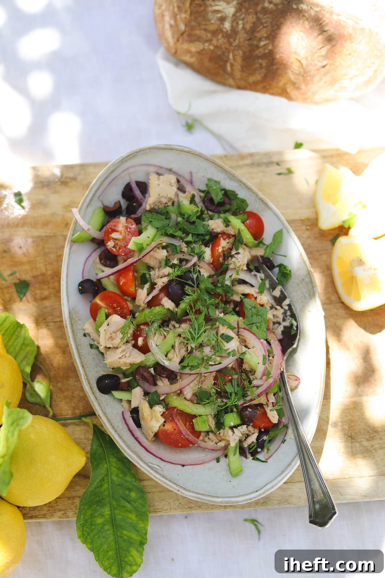 Mediterranean Tuna Salad with Lemon and Sourdough Overhead view of Mediterranean tuna salad with albacore tuna, cherry tomatoes, kalamata olives, celery, red onion, parsley, lemon wedges, and crusty sourdough bread.