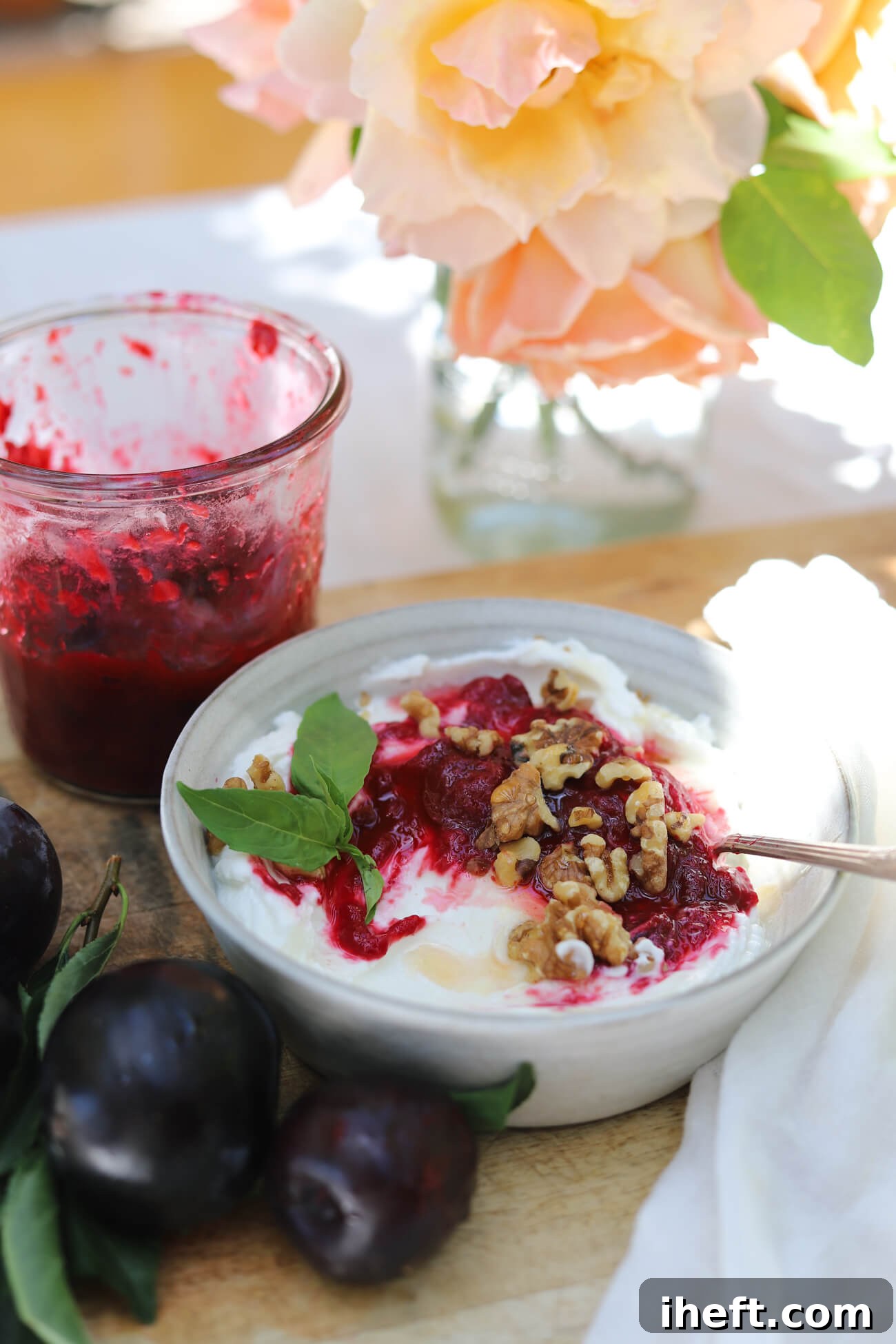 Homemade Roasted Plum Compote with Greek Yogurt Greek yogurt topped with homemade roasted plum compote, walnuts, and fresh basil with a jar of plum compote in the background